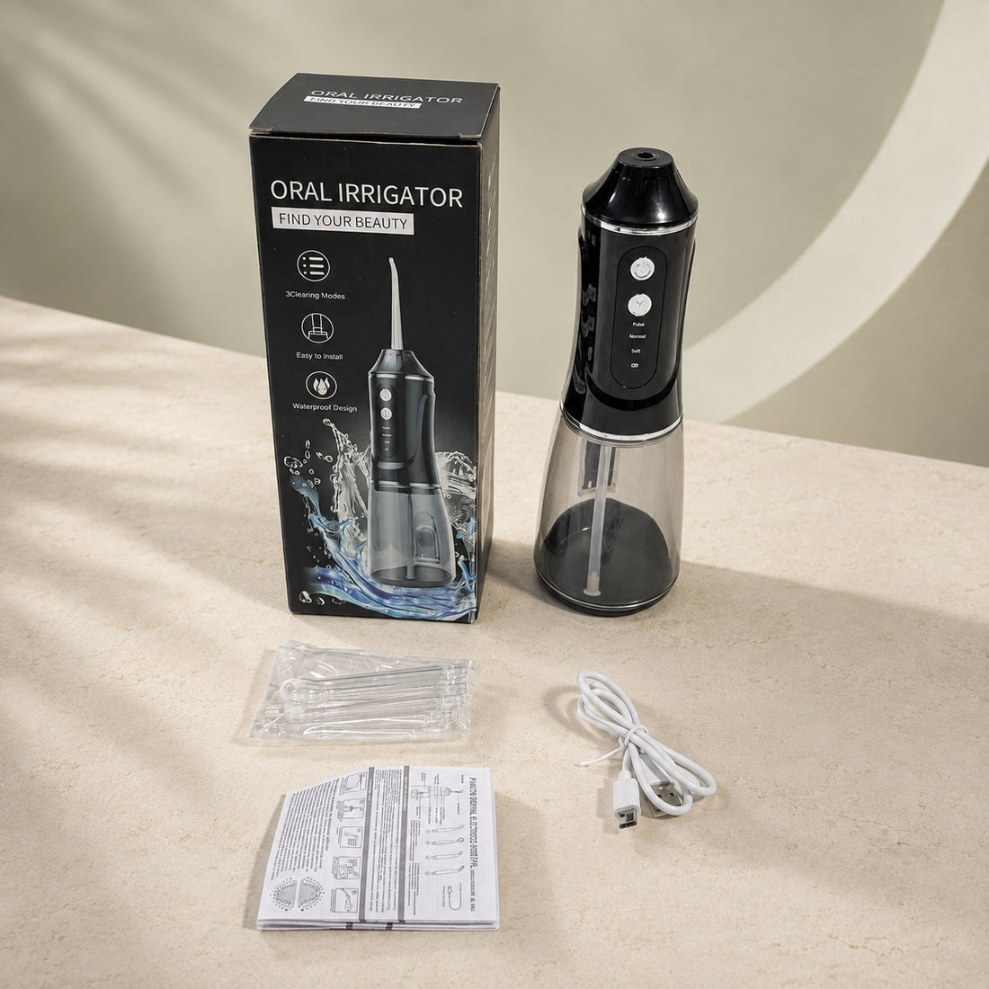 Coffret AquaPulse One Noir Minuit avec appareil, quatre embouts, câble USB et notice, sur fond pierre claire.