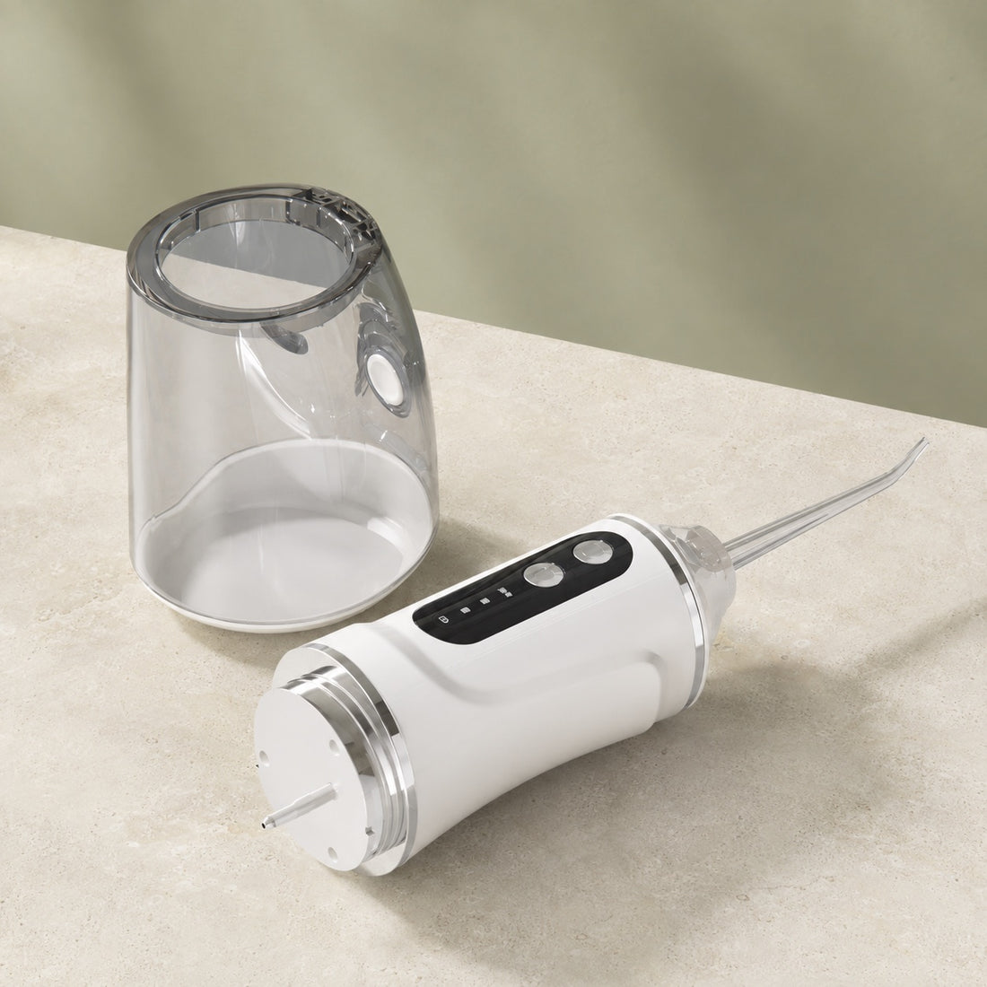 Réservoir amovible transparent détaché de l’hydropulseur AquaPulse One Blanc Nacré, sur une surface en pierre claire.