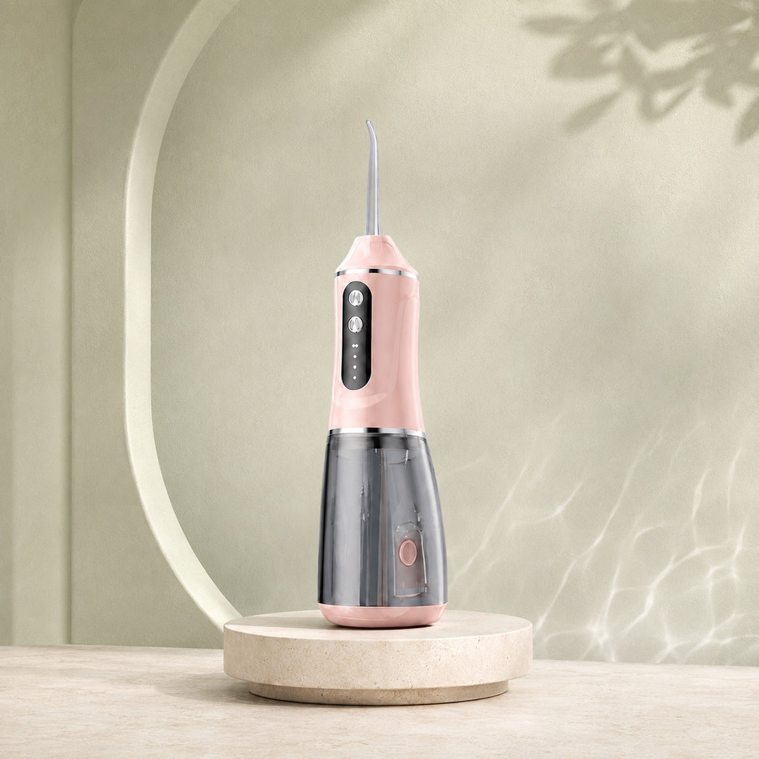 Hydropulseur sans fil ORALYA AquaPulse One Rose Poudré sur un socle en pierre, fond vert sauge.